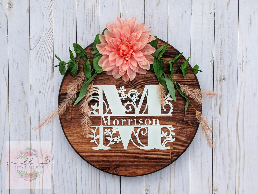 Personalized white last name family monogram on a wood round with coral flowers and greenery